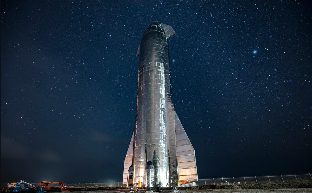 A Starship prototype lit up at night under a starfield at the SpaceX test site